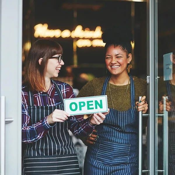Two happy baristas holding an open sign in their coffee shop doorway